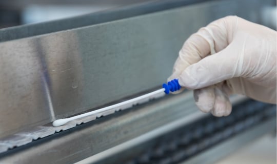 A technician uses a Neogen® Clean-Trace® ATP testing swab on a food conveyor.